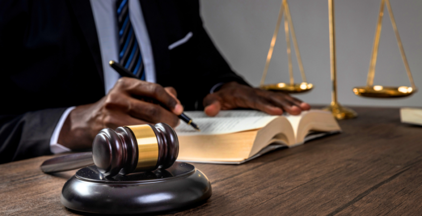 Person sits at a desk with a gavel and a set of scales of justice beside them.